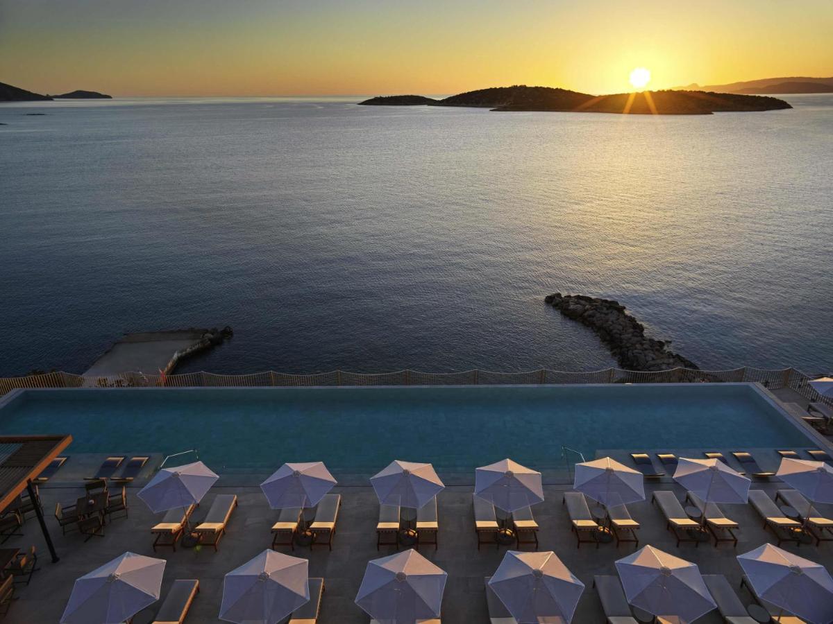 een uitzicht op een zwembad met ligstoelen en de oceaan bij NIKO Seaside Resort MGallery in Agios Nikolaos
