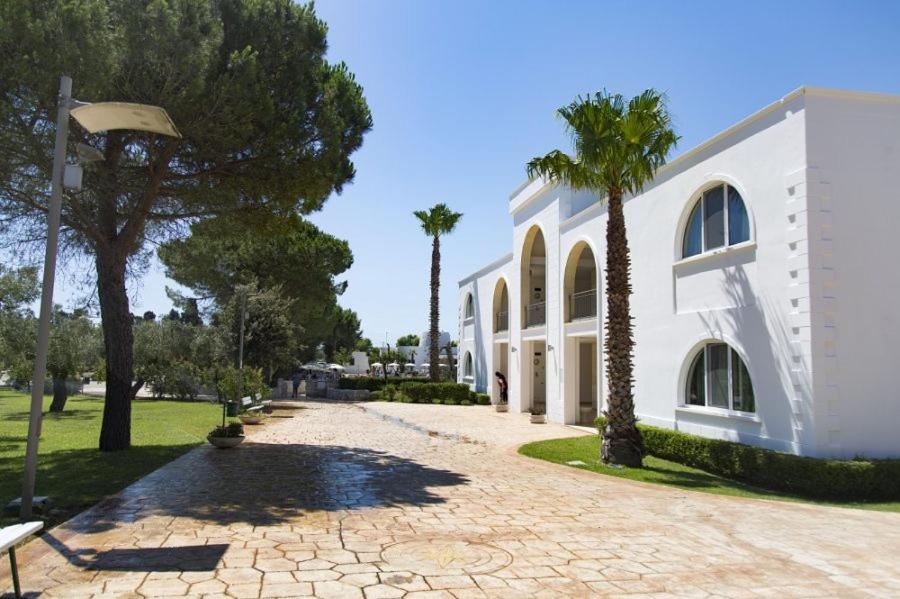 een wit gebouw met palmbomen naast een straat bij Color Dolmen Family Village in Minervino di Lecce