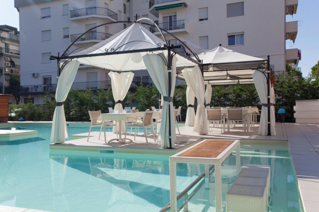 een zwembad met tafels en parasols naast een gebouw bij Ute Hotel in Lido di Jesolo