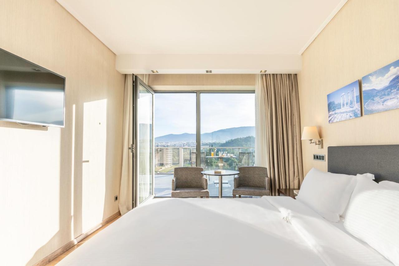 een hotelkamer met een bed en een groot raam bij The Athens Gate Hotel in Athene