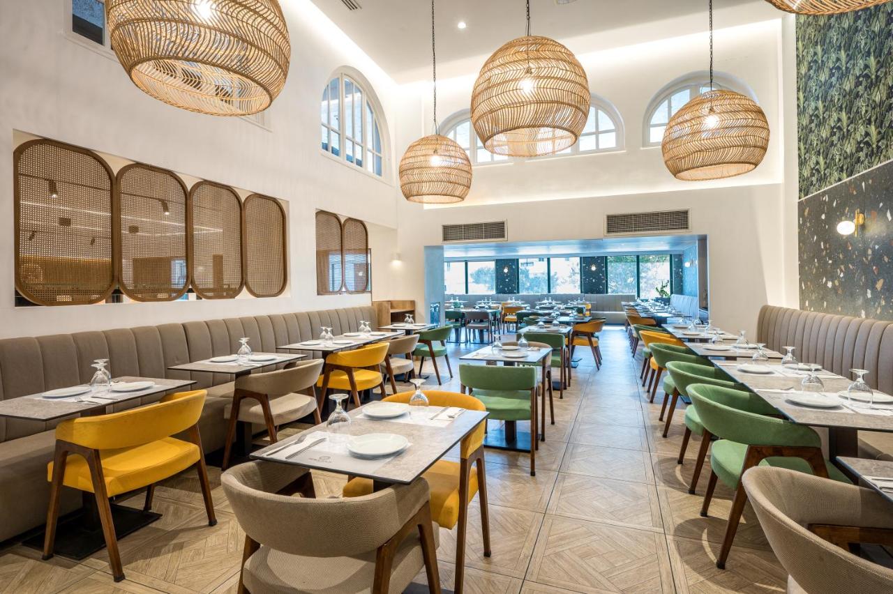 een restaurant met tafels, stoelen en ramen bij Heronissos Hotel in Chersonissos