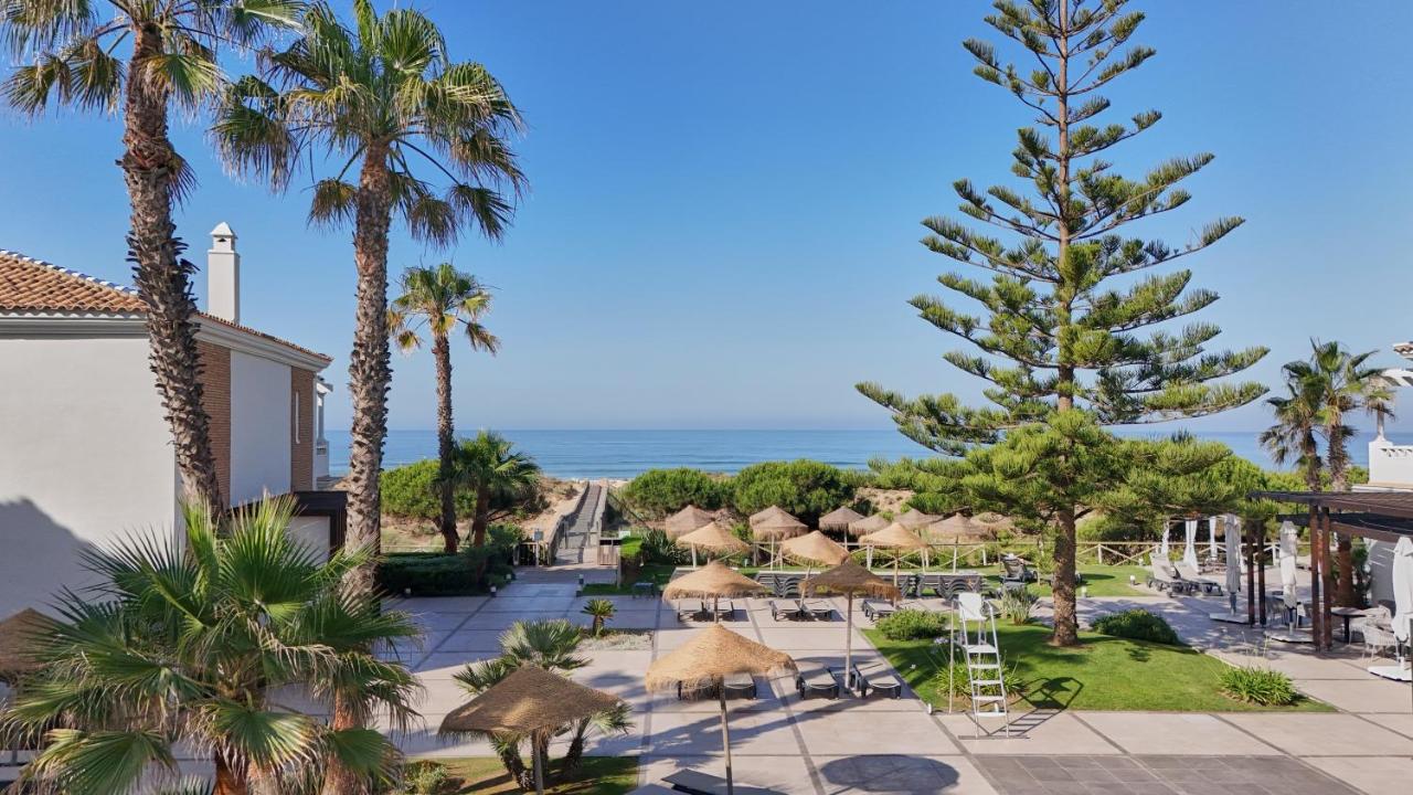 Een uitzicht op het strand vanaf een resort met palmbomen en parasols. bij Barceló Punta Umbría Mar in Punta Umbría