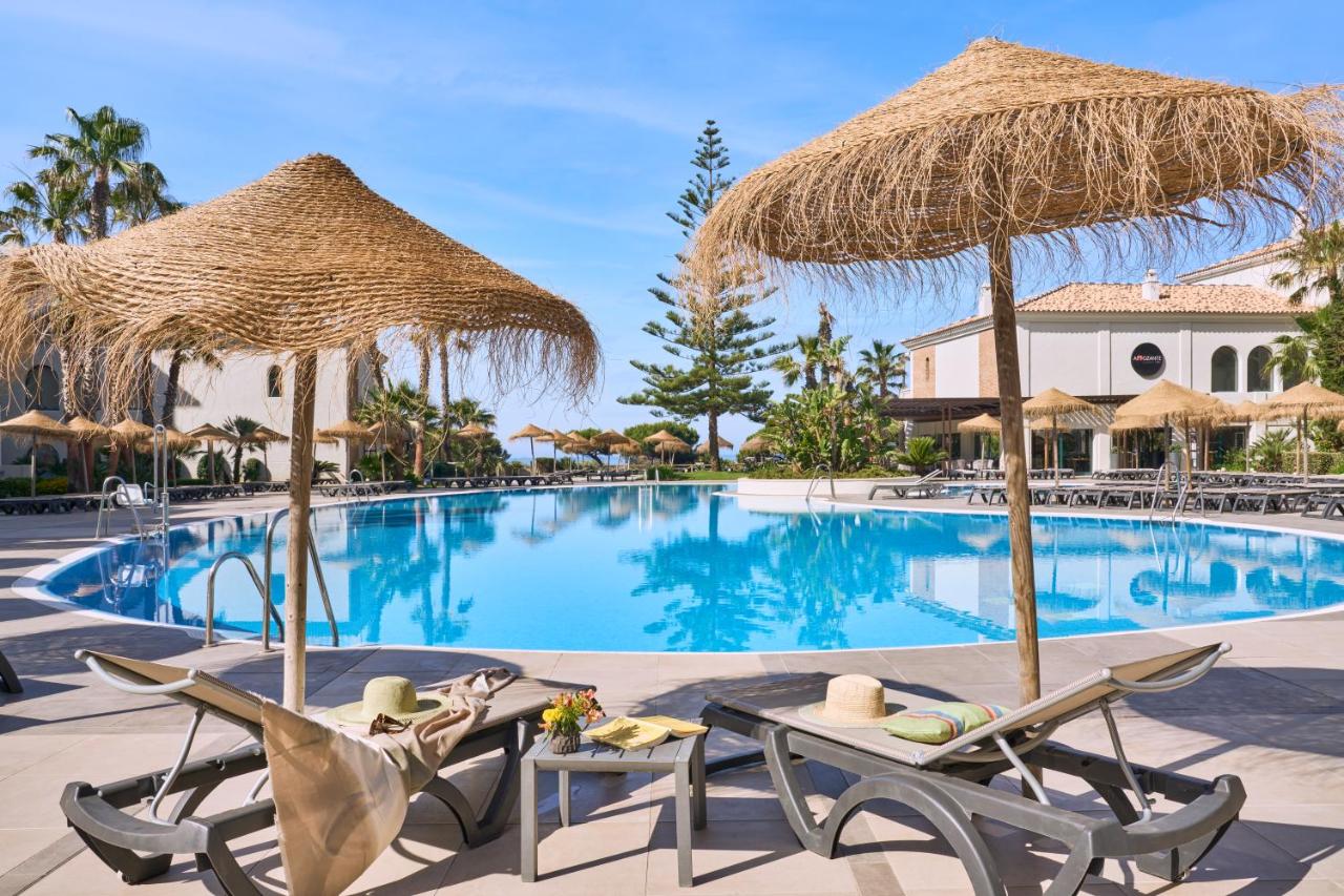 een resortzwembad met twee stoelen en parasols bij Barceló Punta Umbría Mar in Punta Umbría