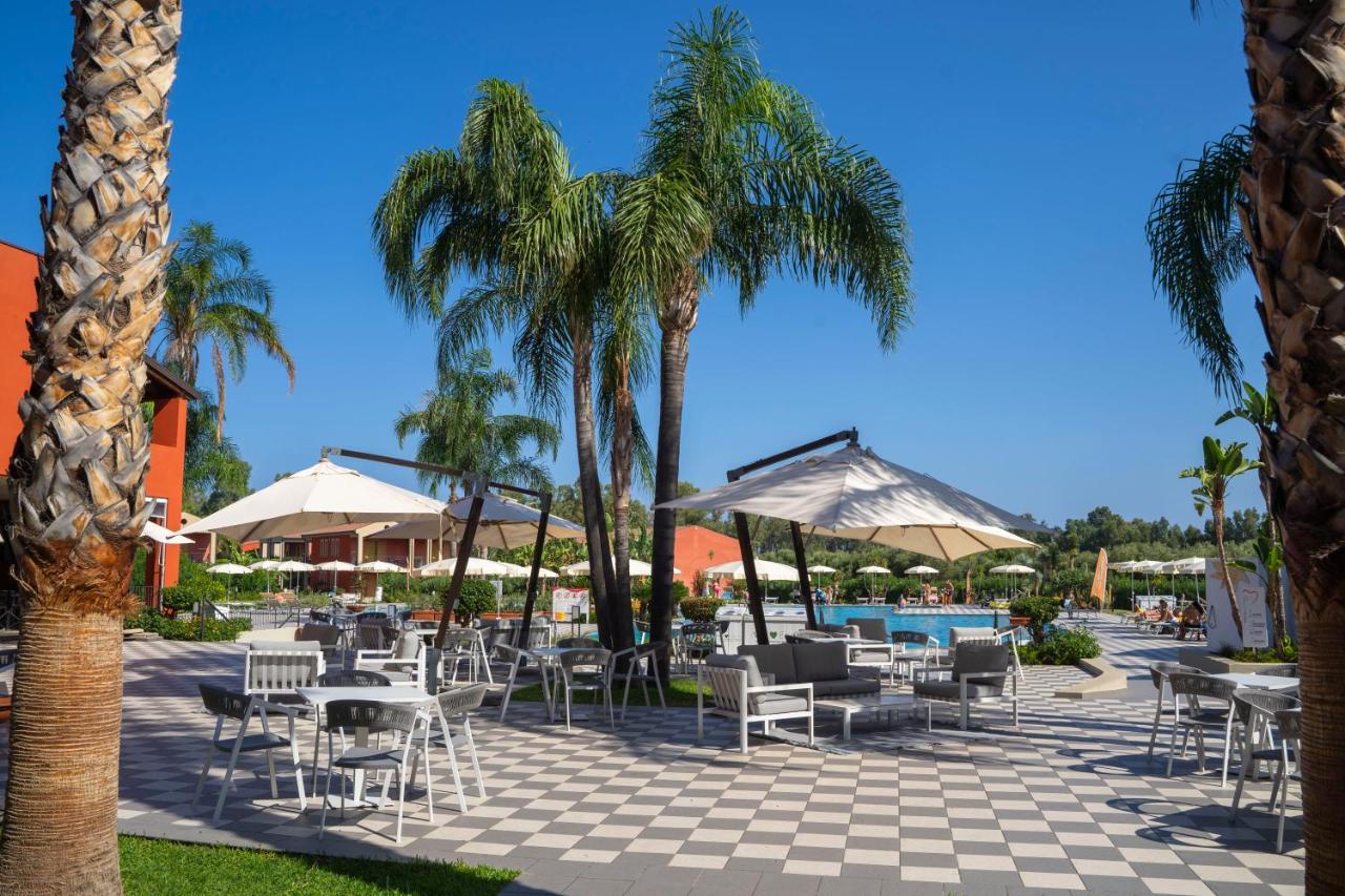 een terras met tafels en stoelen en palmbomen bij VOI Baia di Tindari Resort in Furnari