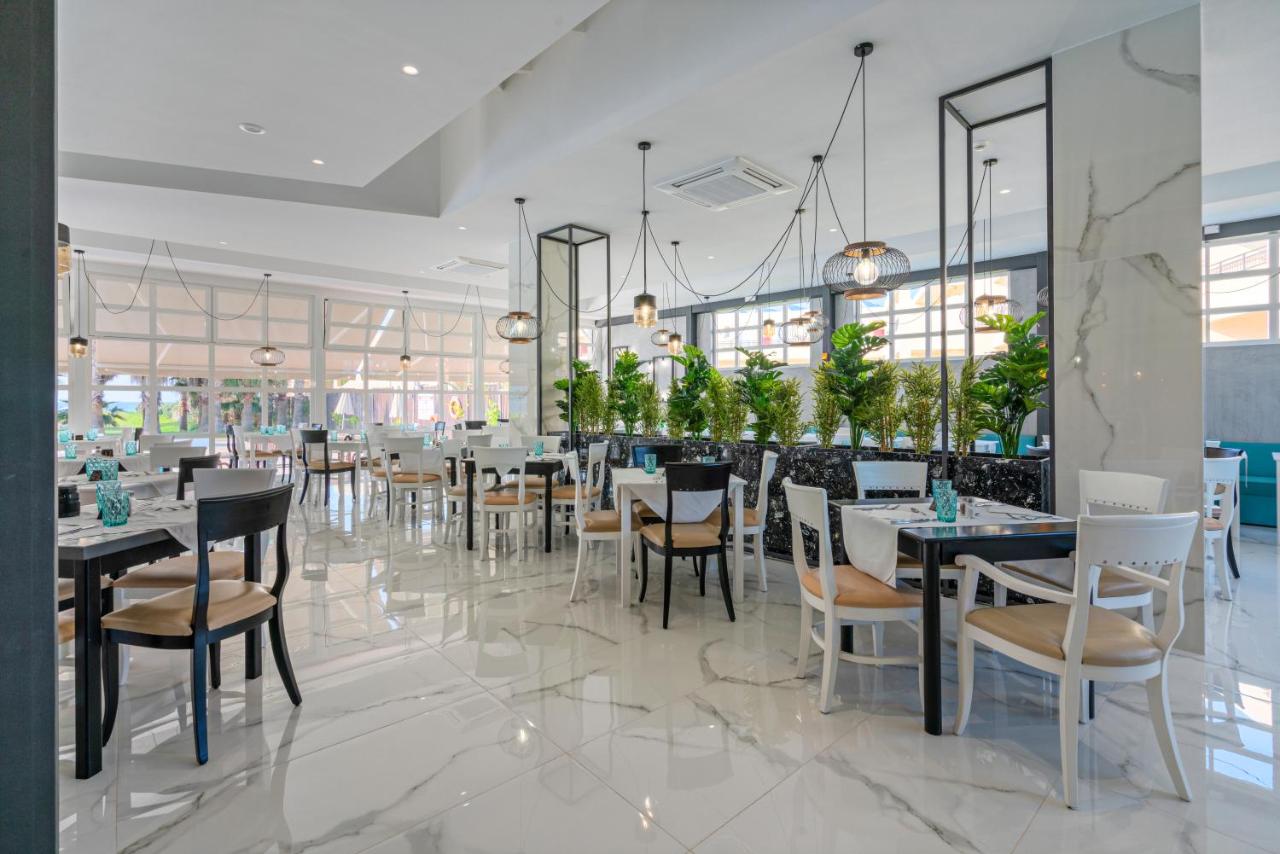 een restaurant met witte tafels en stoelen en planten bij Delfina Tropic Beach - Adults Only in Georgioupolis