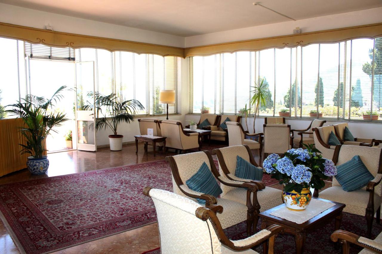 een wachtkamer met stoelen, tafels en ramen bij Hotel Mediterranée in Taormina