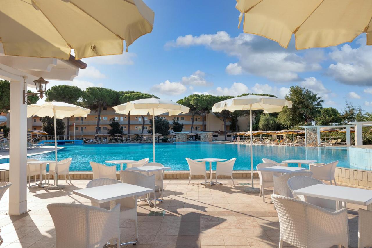 een zwembad met tafels, stoelen en parasols bij Sentido Tirreno Resort in Cala Liberotto