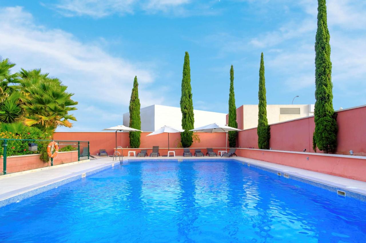 een zwembad met bomen en een gebouw bij Hilton Garden Inn Málaga in Málaga