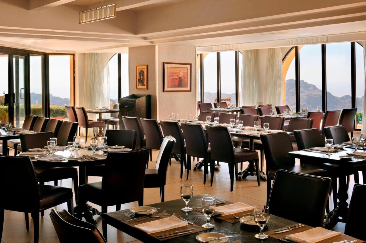 een eetkamer met tafels en stoelen en ramen bij Petra Marriott Hotel in Wadi Musa