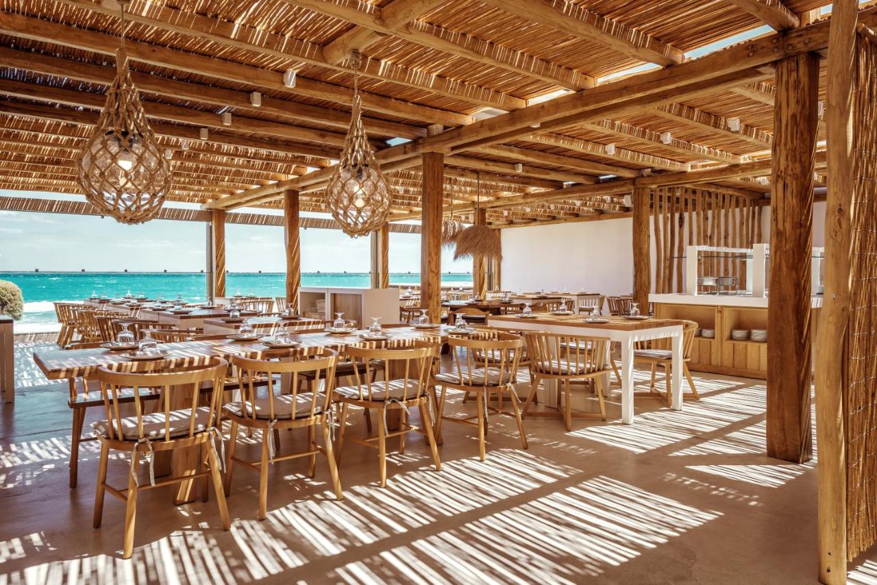 een restaurant met houten tafels en stoelen en uitzicht op de oceaan bij Mitsis Selection Rinela in Kokkíni Khánion
