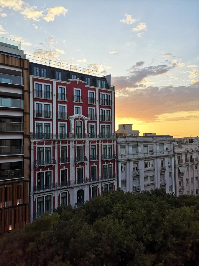 een rood-wit gebouw met een zonsondergang op de achtergrond bij Hotel Nazareth in Lissabon