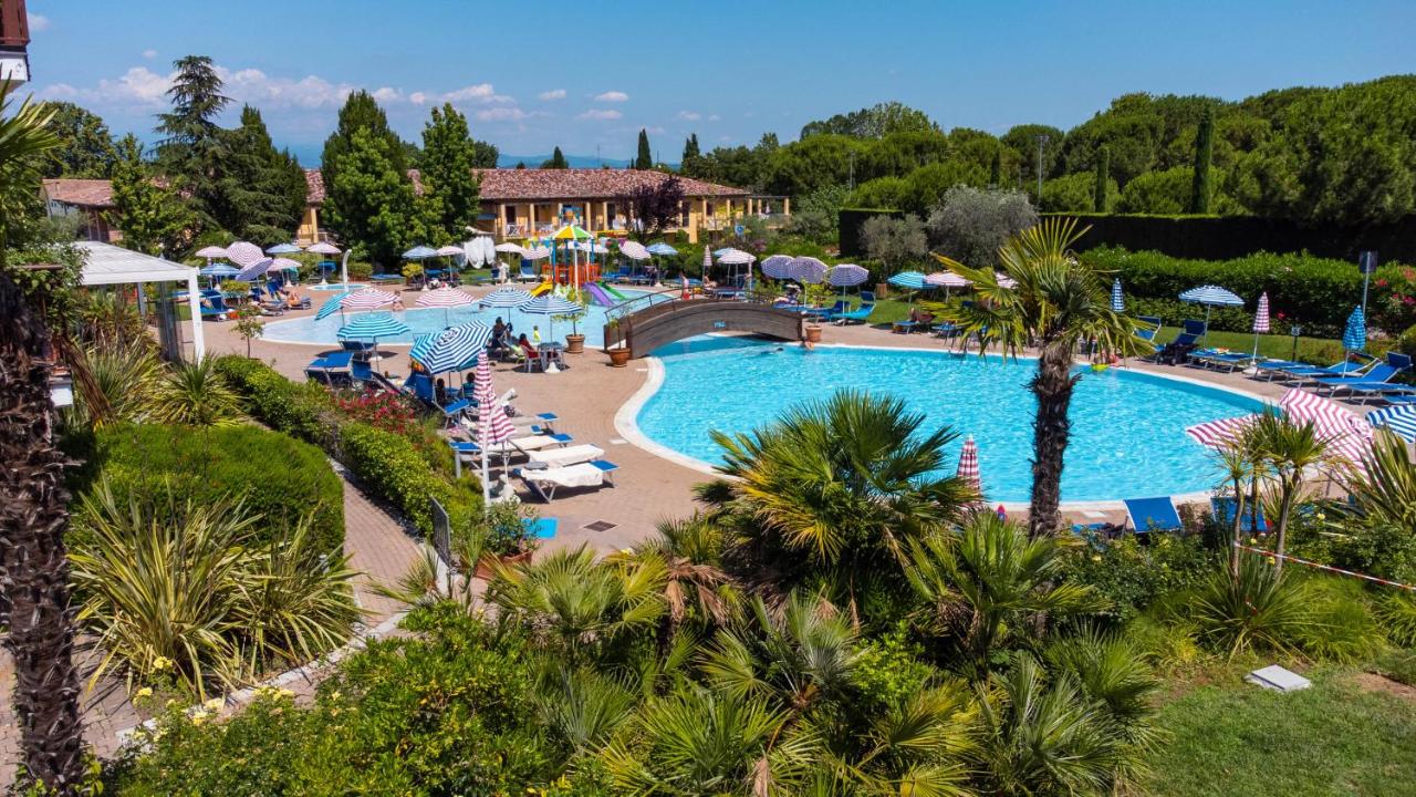 een zwembad bij een resort met palmbomen en parasols bij Hotel Bella Italia in Peschiera del Garda