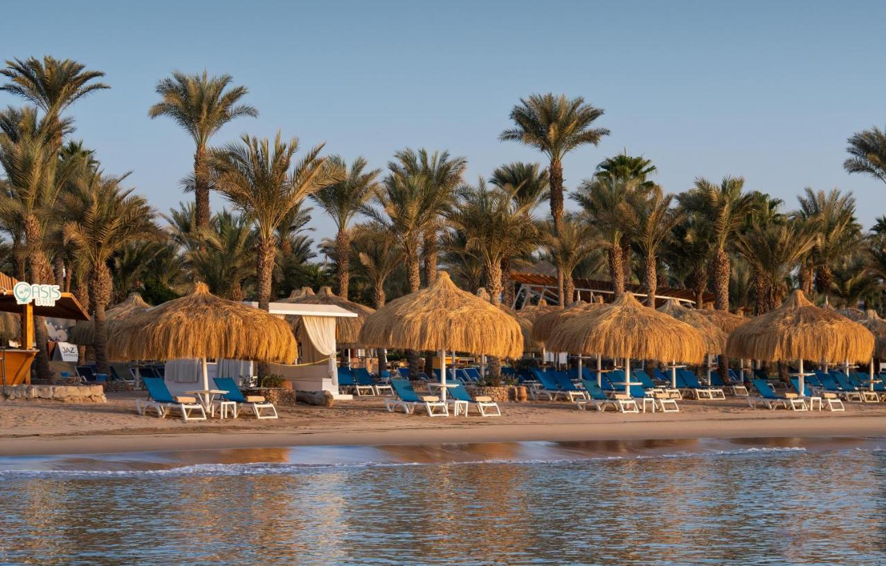 een strand met stoelen, parasols van stro en palmbomen bij JAZ Fayrouz in Sharm El Sheikh