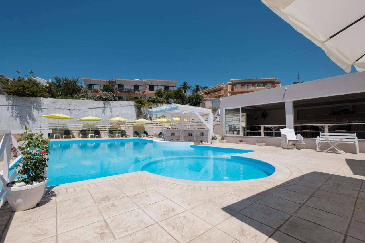 een zwembad met blauw water en parasols bij Kouros Apartments & Studios By Hotelius in Agios Stefanos
