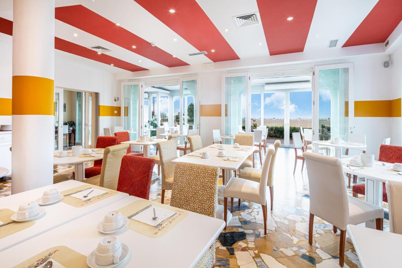een restaurant met witte tafels en stoelen en ramen bij Hotel Karinzia in Caorle
