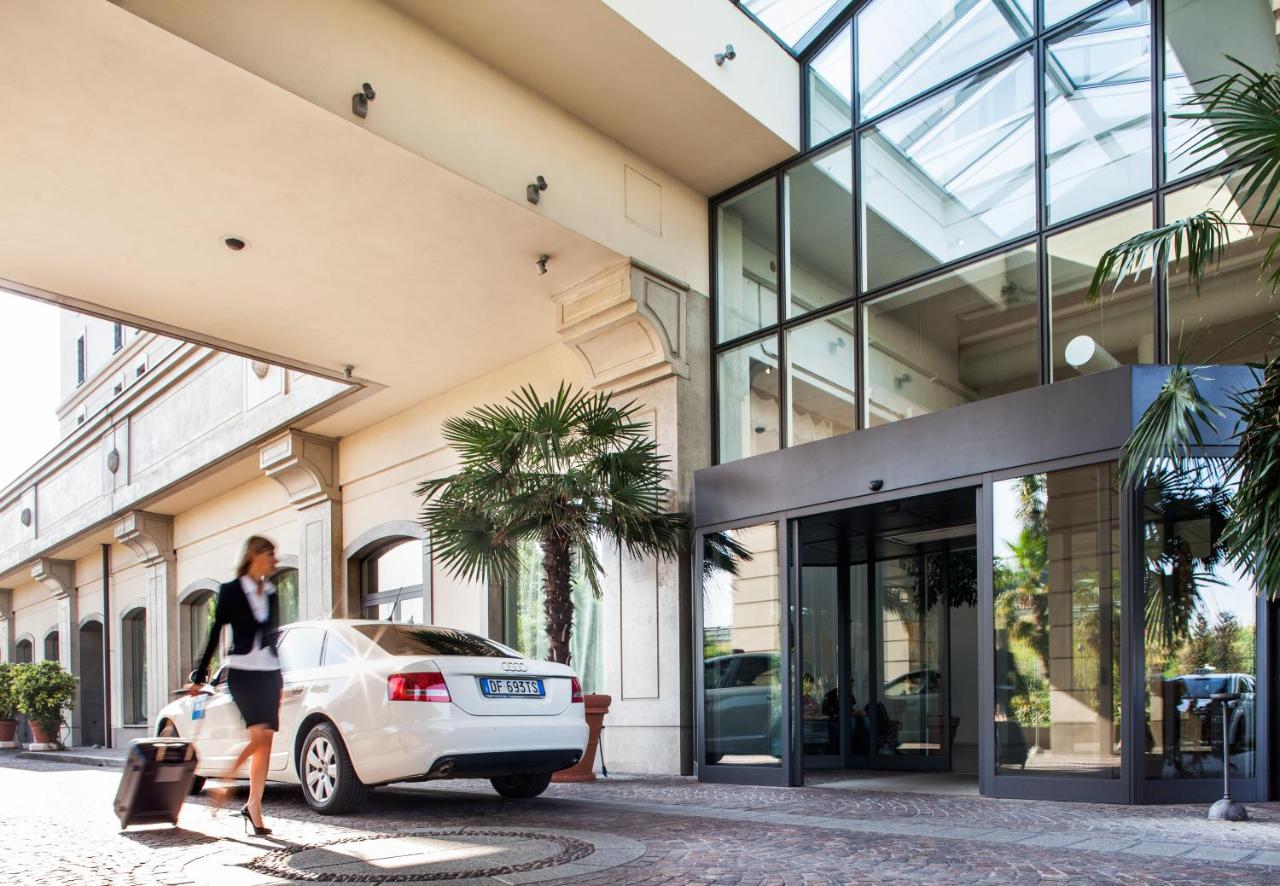 een vrouw loopt langs een witte auto voor een gebouw bij Cosmo Hotel Palace in Cinisello Balsamo