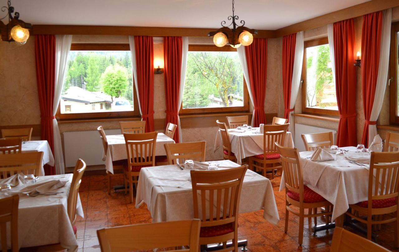 een restaurant met witte tafels en stoelen en ramen bij Hotel Stella Alpina in Bellamonte